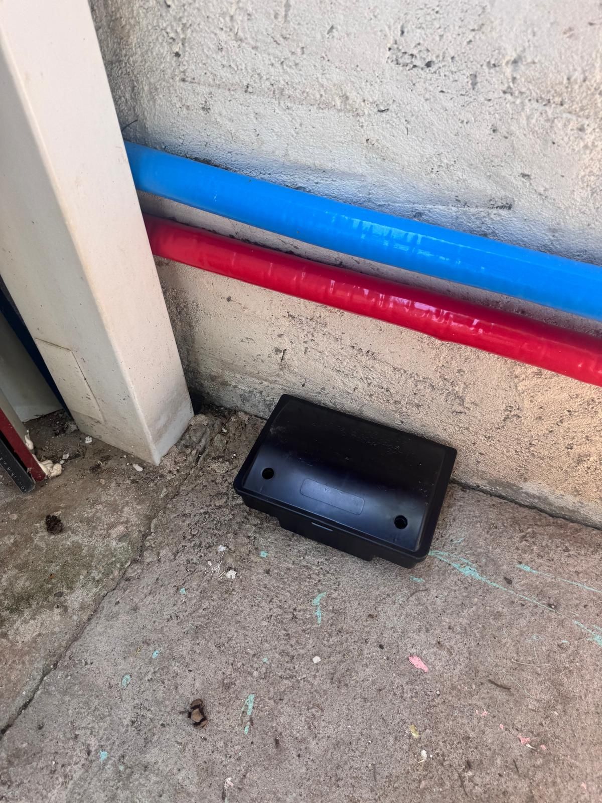 Estación portacebos negra instalada junto a una pared, en zona de paso de roedores